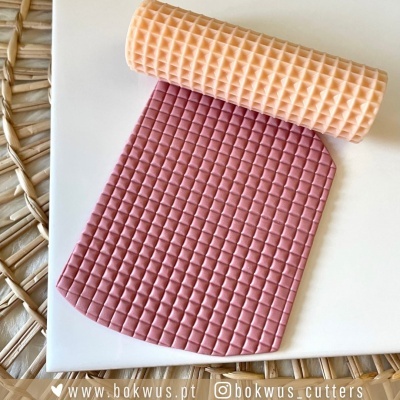Rolo texturizador cor pêssego e massa rosa com padrão quadriculado sobre superfície branca