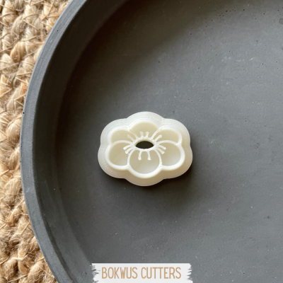 Forma de corte para biscoitos em plástico branco com formato de flor sobre prato cinzento escuro