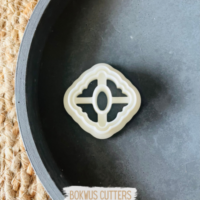 Cortador de massa branco com design geométrico numa superfície escura circular ao lado de tapete de fibra natural