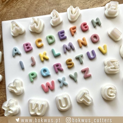 Conjunto de cortadores de letras do alfabeto em plástico branco com letras coloridas em tons pastel.