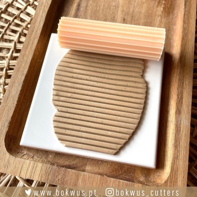 Rolo de massa com textura de riscas em placa branca sobre tabuleiro de madeira