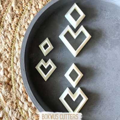 Conjunto de cortadores brancos em formas geométricas numa bandeja cinza sobre tapete natural com etiqueta BOKWUS CUTTERS