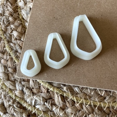 Três anilhas plásticas brancas em forma de gota sobre superfície castanha e tapete de fibras.