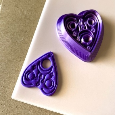 Moldes de impressão 3D roxos em forma de coração com texturas internas, sobre superfície branca e fundo castanho