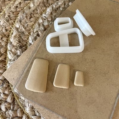 Cinco peças plásticas, três bege trapezoidais e duas brancas, sobre papel castanho e superfície trançada.