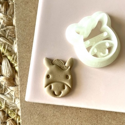 Cortador e carimbo de biscoitos em forma de cabeça de vaca branca e massa marrom claro sobre fundo rosa e castanho