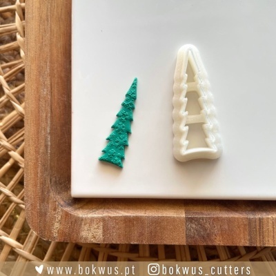Cortador de massa branco e massa verde cortada em forma de árvore de Natal sobre prato branco e tabuleiro de madeira