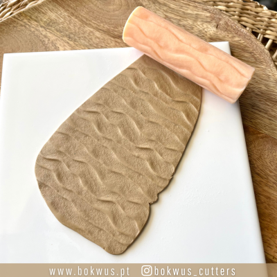 Rolo de madeira texturizado e massa marrom clara sobre superfície branca