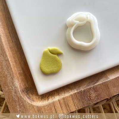 Cortador de bolachas em forma de pêra com bolacha amarela e tábua de madeira