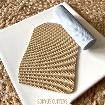 Cortador de massa bege texturizado e rolo branco sobre prato branco e mesa castanha texturizada