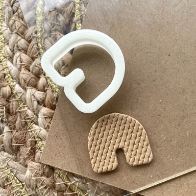 Dois cortadores de biscoito em formato de letra, um branco e outro castanho texturizado, sobre papel castanho e tecido trançado.