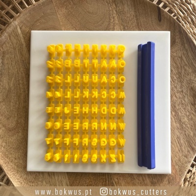 Cortadores de biscoitos amarelos em letras e números com régua azul sobre base branca em fundo de madeira