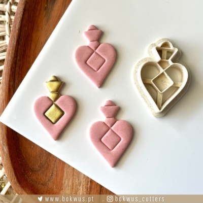 Moldes em forma de coração com detalhes geométricos rosa e dourados e cortador branco sobre superfície branca