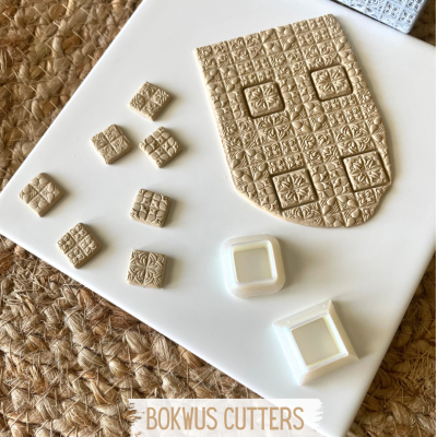 Cortadores de massa creme com padrões geométricos e florais sobre superfície branca e tapete de fibra