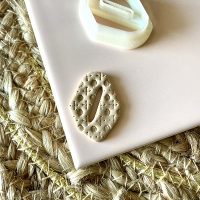 Objeto de cerâmica bege com padrão floral sobre suporte branco e tecido trançado