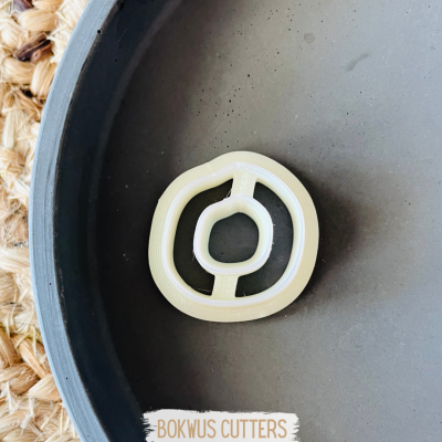 Cortador de biscoitos plástico branco com formato irregular numa superfície preta