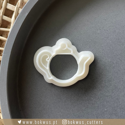 Cortante branco translúcido em forma de chávena numa superfície preta ao lado de uma cesta de vime