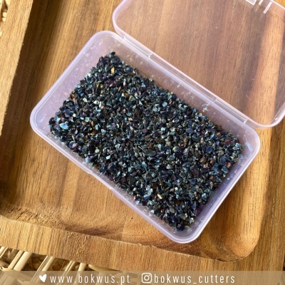 Caixa plástica com pequenas pedras escuras iridescentes sobre bandeja de madeira