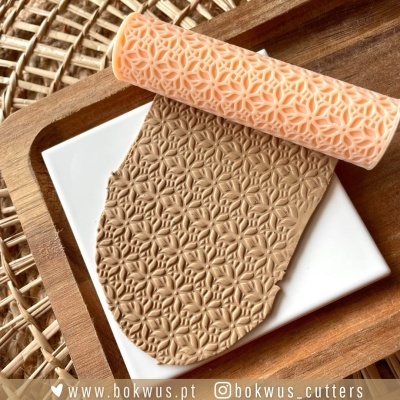 Rolo de massa com padrão floral em relevo sobre base branca e madeira