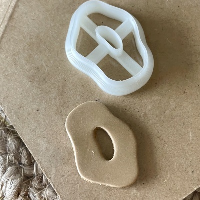 dois objetos com formas orgânicas, um branco translúcido e outro bege cerâmico, sobre superfície castanha