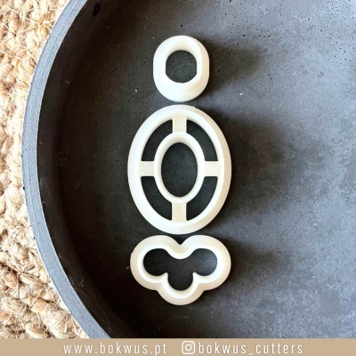 Três cortadores de massa brancos em formas geométricas sobre travessa cinzenta