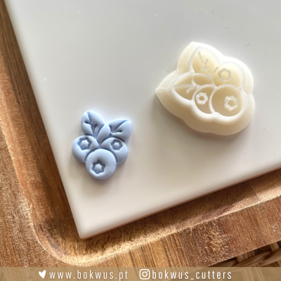Moldes para biscoitos de silicone com design de frutos em azul claro e branco sobre superfície branca e base de madeira clara