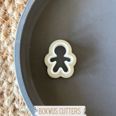 Cortador de biscoitos em forma de boneco branco sobre prato cinzento e tapete de palha