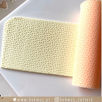 Rolo de massa texturizada com padrão de corações pequenos em relevo sobre superfície branca