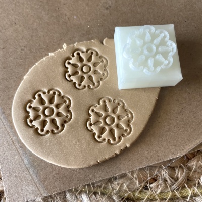 Carimbo de silicone branco flor geométrica sobre massa de modelar castanha e cartão