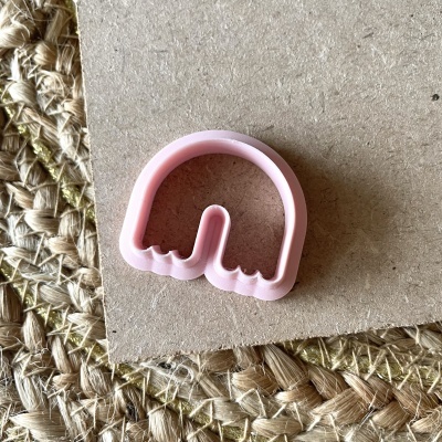 Cortador de bolachas rosa claro em cartão sobre tapete de fibras naturais.