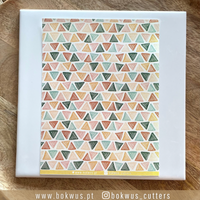 Conjunto de cortadores de bolachas triangulares com padrão geométrico colorido sobre azulejo branco e fundo de madeira.