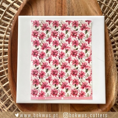 Azulejo quadrado com padrão floral rosa, vermelho e branco sobre placa branca, colocado numa travessa de madeira em superfície de ráfia.
