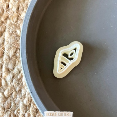 Fivela em forma de caracol branca e amarela num recipiente cinzento sobre superfície trançada bege.