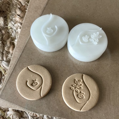 Carimbos de plástico branco com rosto feminino e impressões em argila bege sobre base de madeira