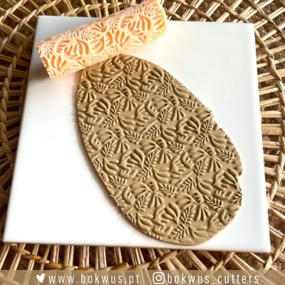 Rolo de textura em silicone com padrão de folhas com massa moldável estampada sobre azulejo branco