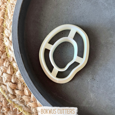 Cortador de bolacha branco em superfície cinza escura sobre tapete trançado.