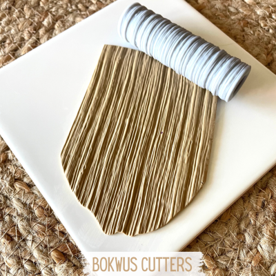 Ferramenta para cortar noodles com rolo branco sobre base branca em fundo de juta