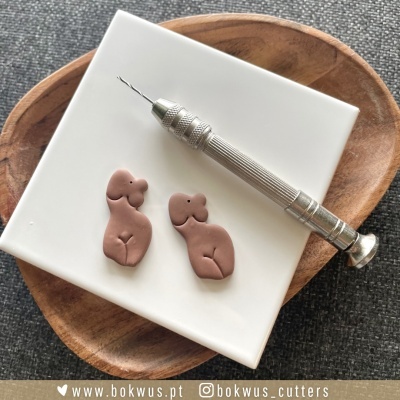 Pendentes femininos castanhos e instrumento prateado sobre base branca e tábua de madeira