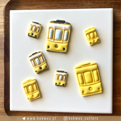 Seis miniaturas de elétricos amarelos e brancos sobre base branca e fundo de madeira