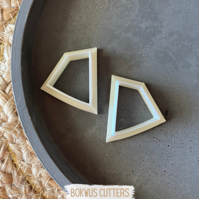 Dois cortadores de massa creme em formato geométrico sobre superfície escura com etiqueta BOKWUS CUTTERS