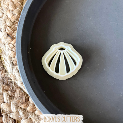 Cortador de biscoitos em forma de concha bege dentro de um prato cinza sobre superfície trançada.