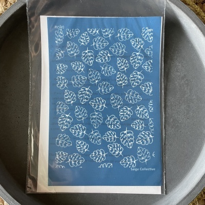 Postal azul com padrão de folhas brancas embalado em saco plástico dentro de tigela cinza