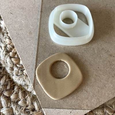 Dois moldes de corte para artesanato em plástico branco e material bege sobre cortiça e tecido rústico.