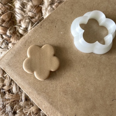 Cortador de massa branco em forma de flor com massa castanha ao lado sobre papel castanho e base de corda trançada