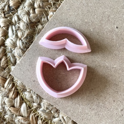 Dois cortadores de plástico rosa em forma de pétalas sobre fundo de papel bege e tecido trançado