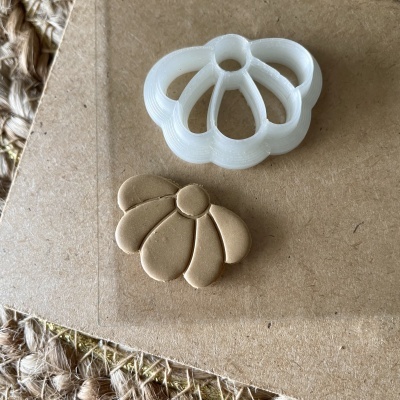 Cortador de massa branco em formato de flor com peça de massa dourada modelada ao lado