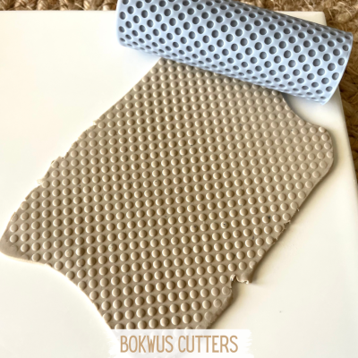 Rolo texturizador azul claro de silicone com padrão de bolhas em massa bege.