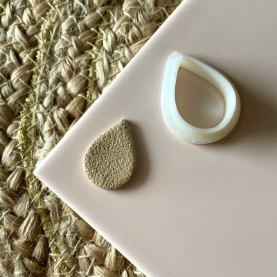 Molde branco e recorte bege em forma de gota sobre superfície rosa e tapete de fibra