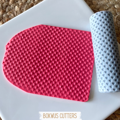 Manta texturizada rosa com padrão de corações ao lado de rolo texturizado cinza claro sobre superfície branca