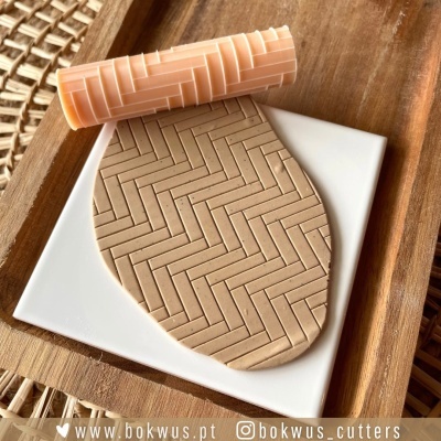 Rolo de massa com padrão geométrico e massa moldada com padrão semelhante sobre placa branca e madeira